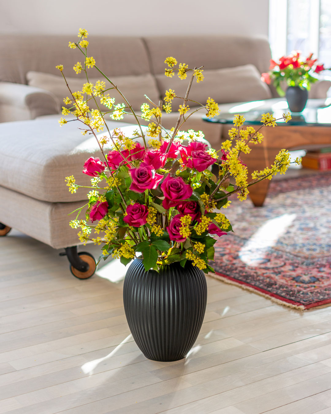 Sort vase i keramik fra Michael Andersen på stuegulv med gule kirsebærkornel blomster og ceriserøde roser