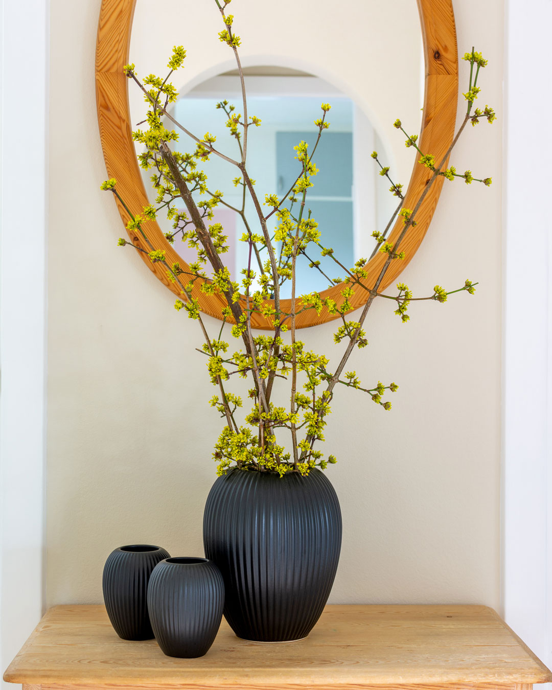 Sorte keramikvaser fra Michael Andersen på skænk i entré med kirsebærkornelgrene med gule blomster